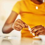 Hands of African female with HIV and Aids at home blood self test kit sitting at a desk waiting to check for results.