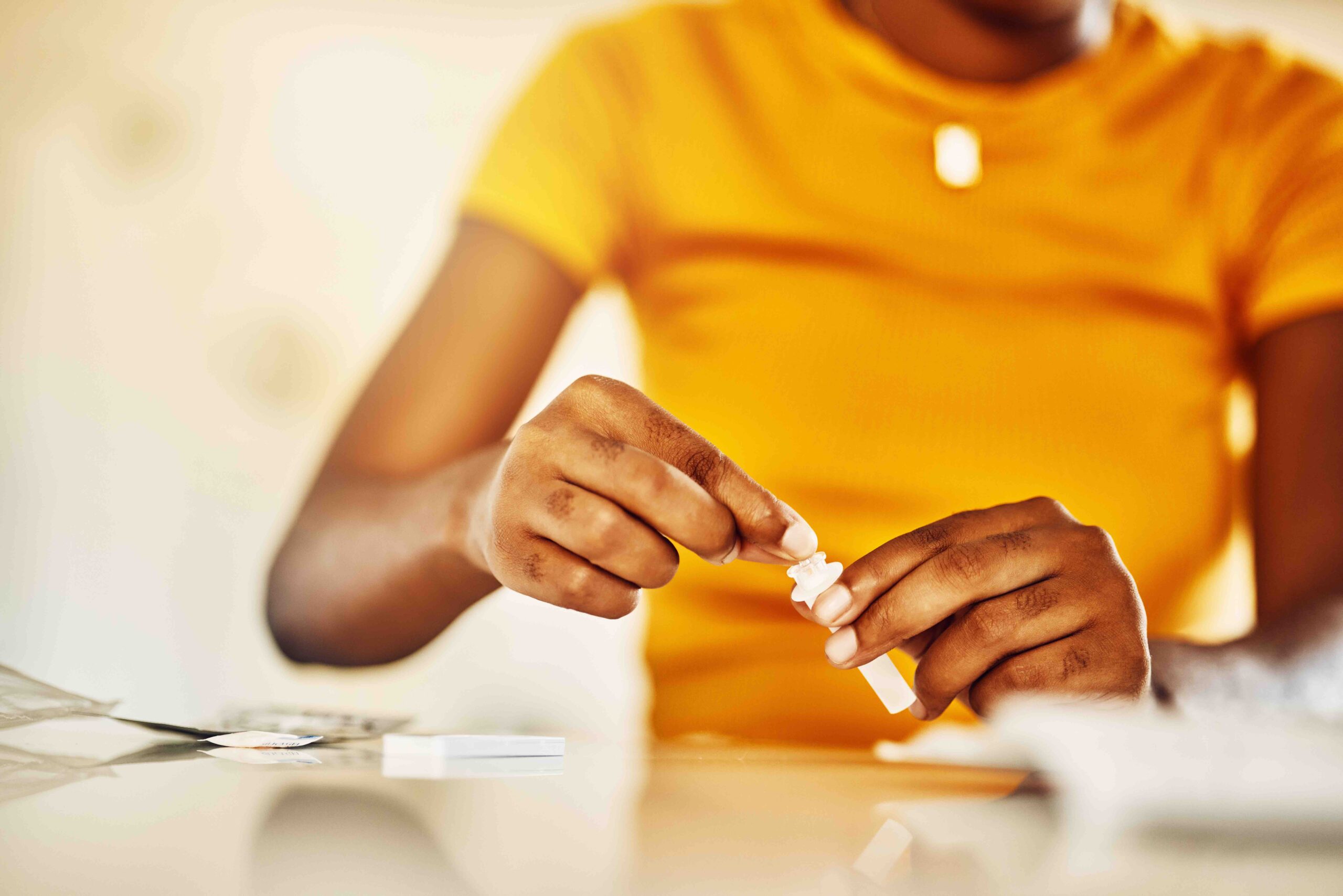 Hands of African female with HIV and Aids at home blood self test kit sitting at a desk waiting to check for results.