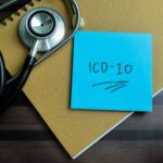 "ICD-10" written on a sticky note, next to a stethoscope, on a wooden table.