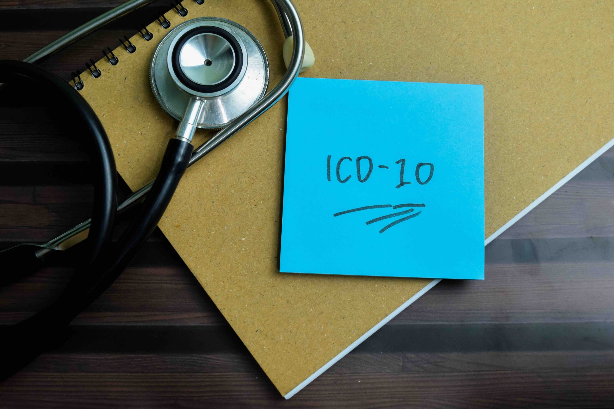 "ICD-10" written on a sticky note, next to a stethoscope, on a wooden table.