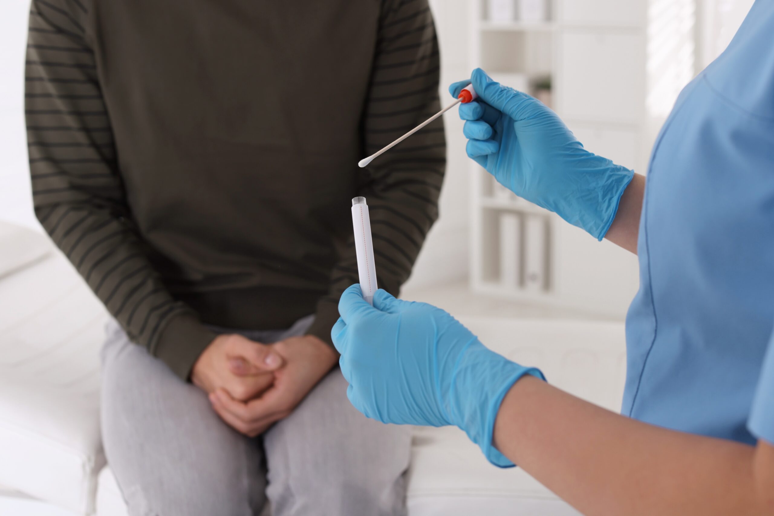 Doctor taking sample for STD testing from man in clinic, closeup