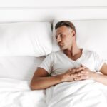 Upset man laying in bed and looking away at an empty pillow