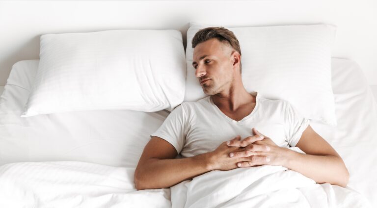 Upset man laying in bed and looking away at an empty pillow