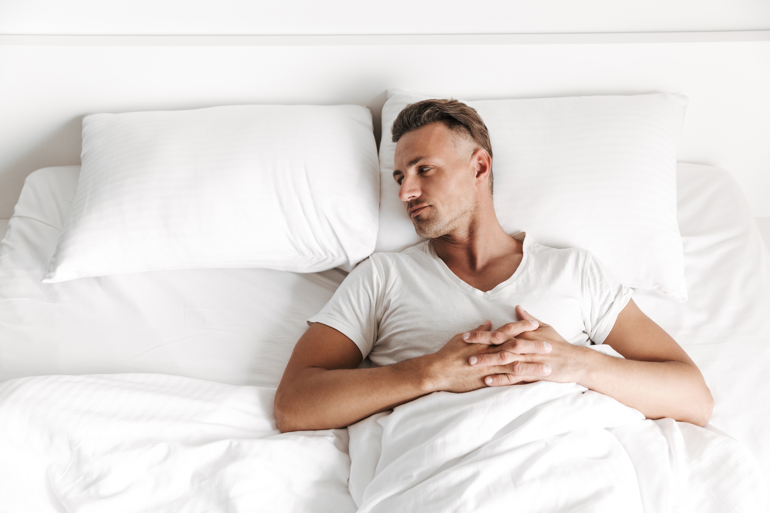 Upset man laying in bed and looking away at an empty pillow