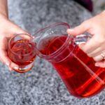 Woman pouring healthy red cranberry juice from bottle into glass, close up.