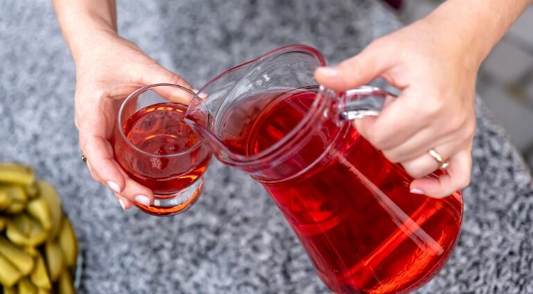 Woman pouring healthy red cranberry juice from bottle into glass, close up.