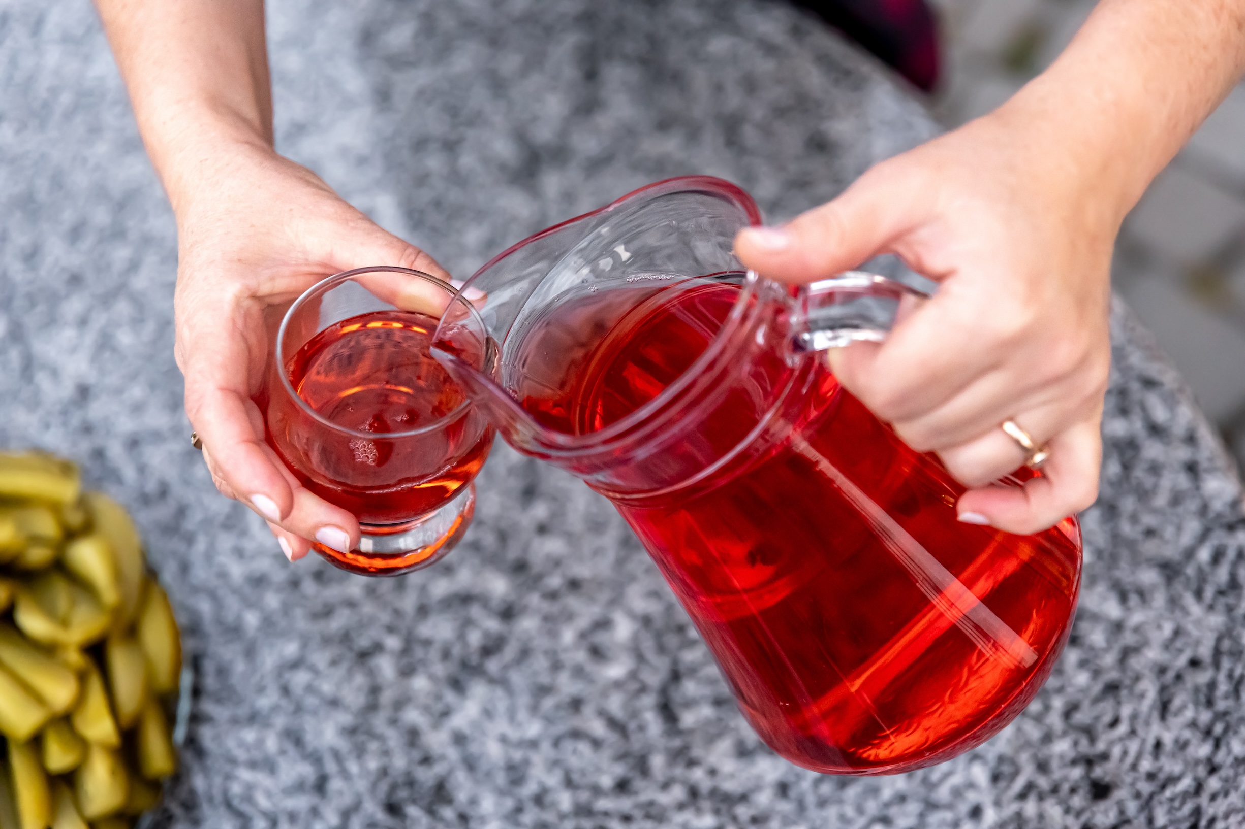 Woman pouring healthy red cranberry juice from bottle into glass, close up.