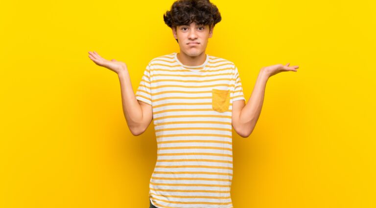 Young man over isolated yellow wall while raising hands, questioning where exactly semen is stored.