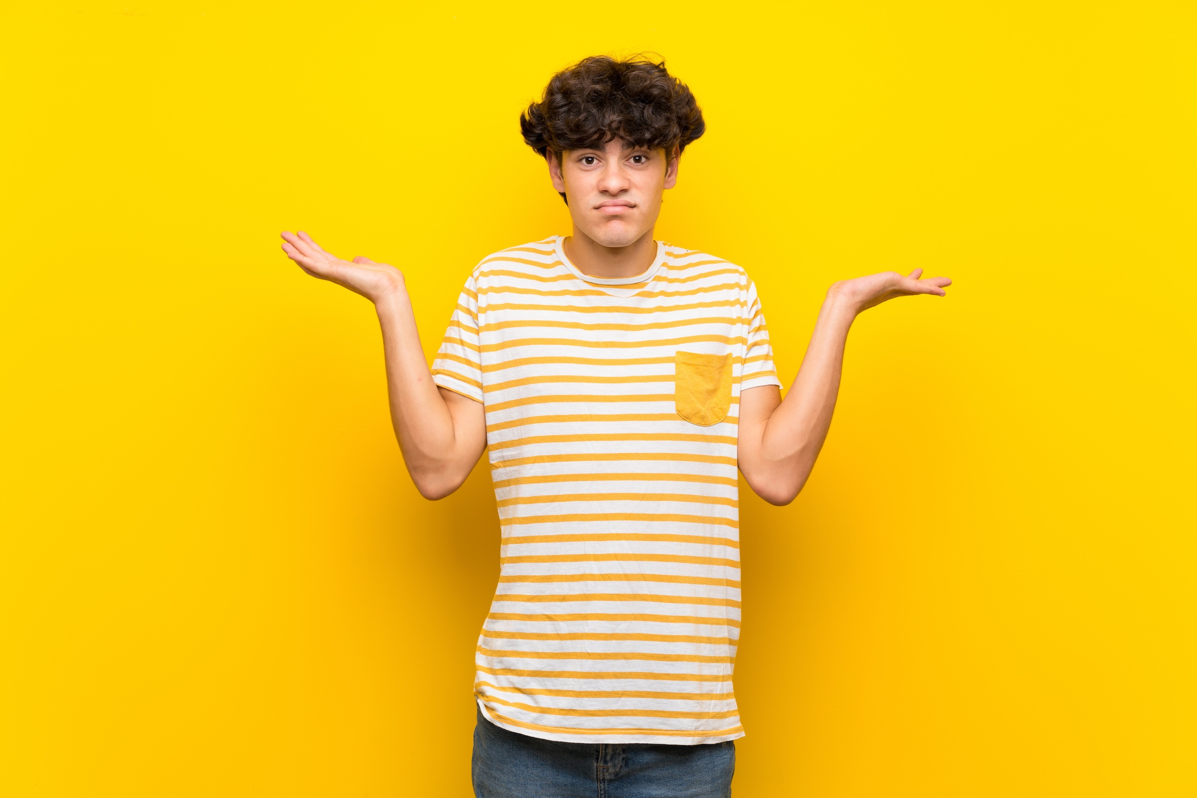 Young man over isolated yellow wall while raising hands, questioning where exactly semen is stored.