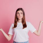 Portrait of young lady holding hands up, mentally comparing the differences between HPV and herpes with a questioning look on her face.