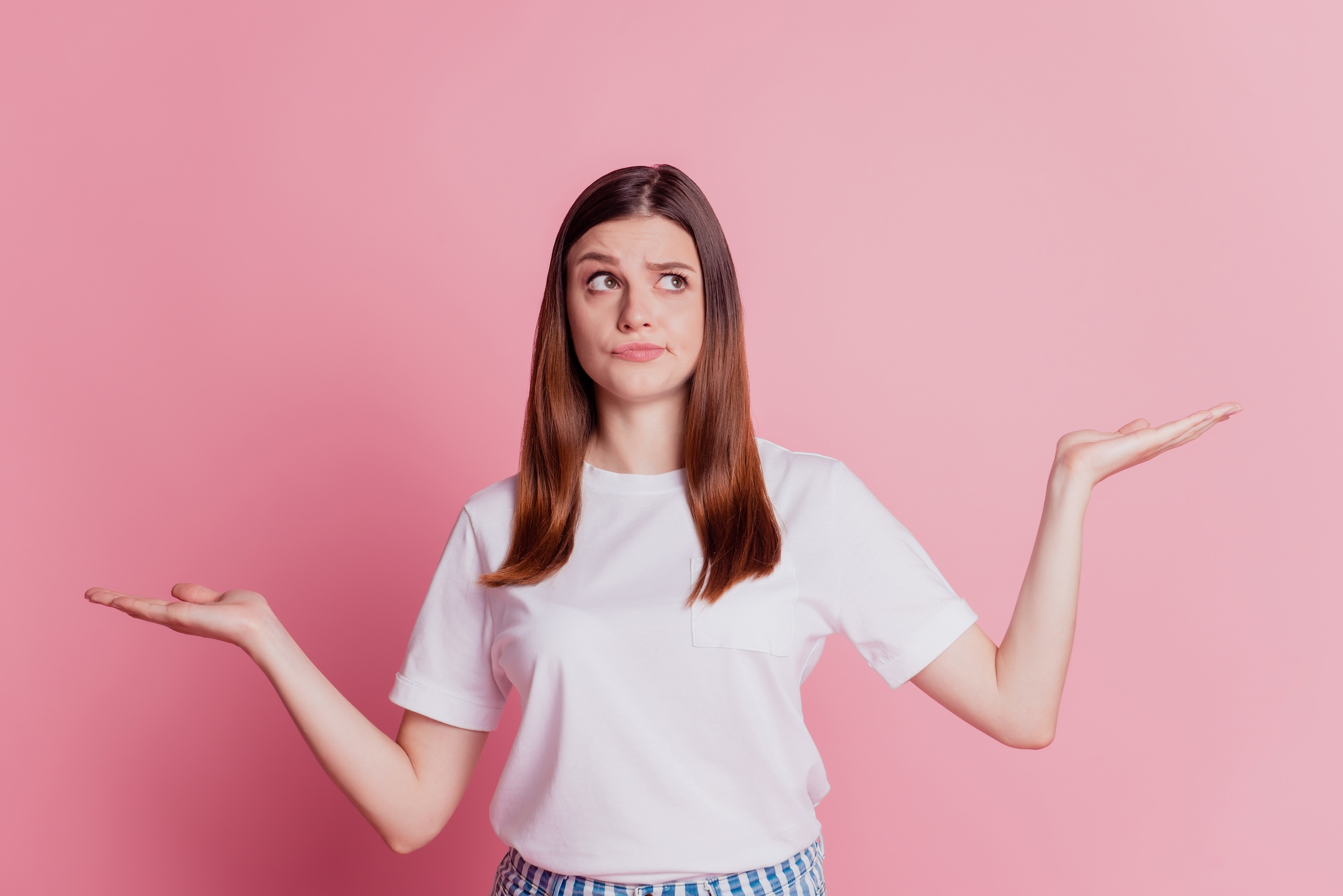 Portrait of young lady holding hands up, mentally comparing the differences between HPV and herpes with a questioning look on her face.