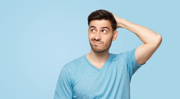 Young doubtful man thinking, scratching head and trying answer whether you can contract chlamydia without sex, isolated on blue background