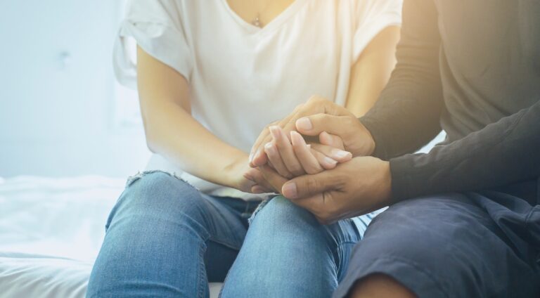 A closeup of couple holding hands, comforting one another during the difficult conversation of an STD diagnosis.