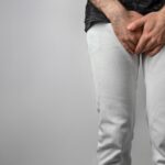 adult male in white pants and dark shirt covering his genital area with his hands in discomfort, potentially due to balanitis.