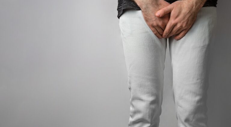 adult male in white pants and dark shirt covering his genital area with his hands in discomfort, potentially due to balanitis.