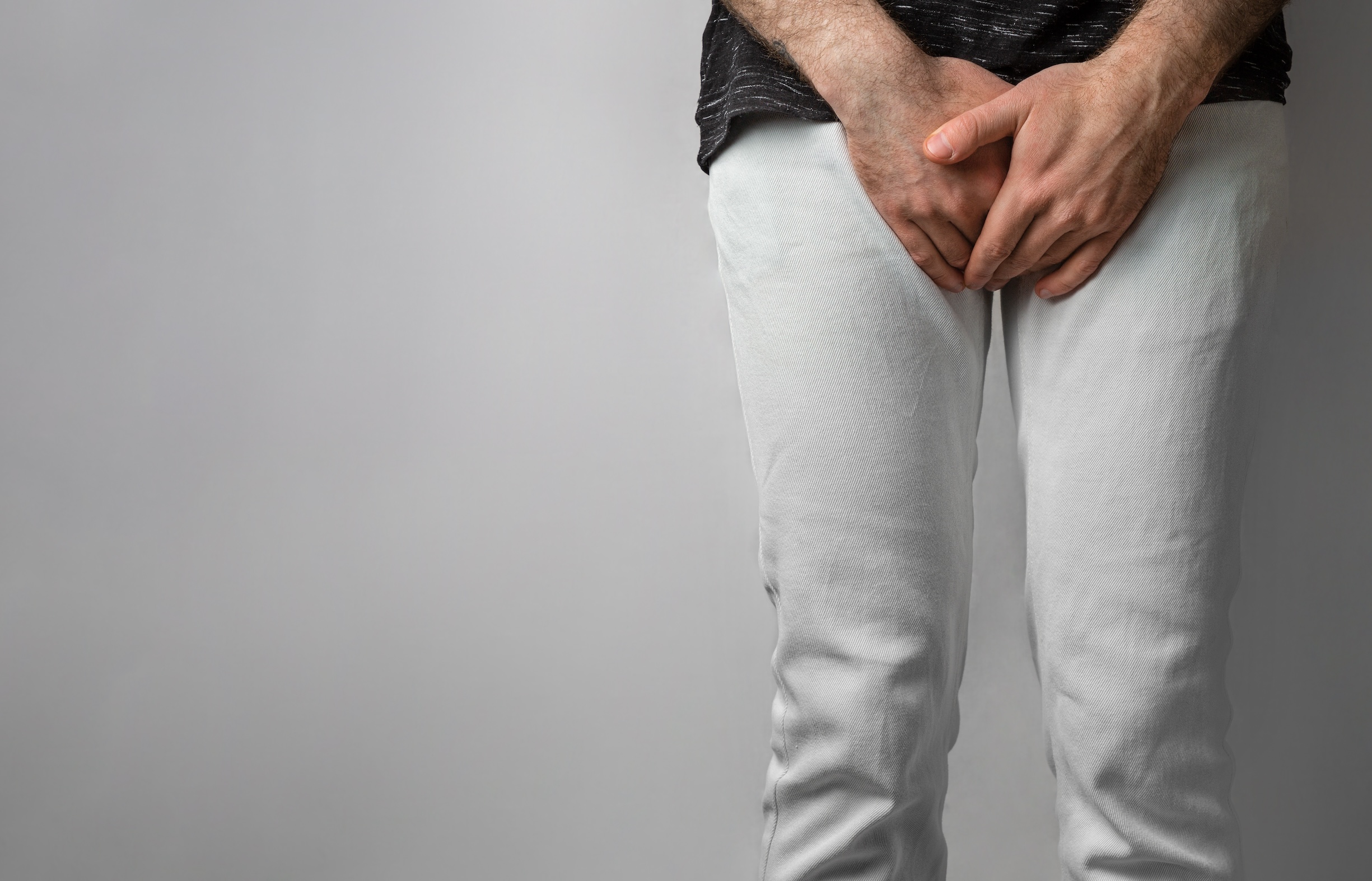 adult male in white pants and dark shirt covering his genital area with his hands in discomfort, potentially due to balanitis.